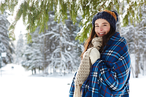 Waist up portrait of smiling young woman posing in winter forest standing under beautiful fir tree and , copy space