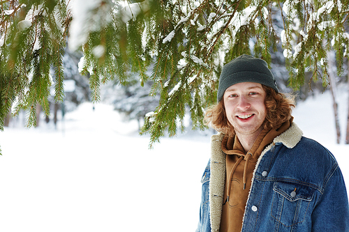 Portrait of modern young man posing in snowy winter forest and  while standing under fir tree, copy space