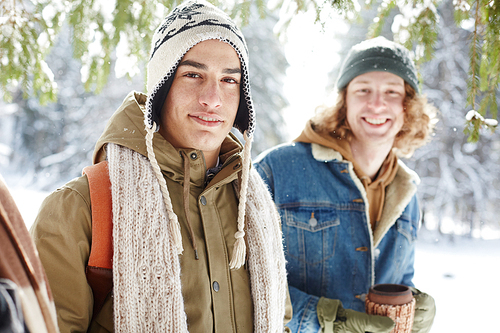 Portrait of two smiling young men posing in winter resort standing in snowy forest and 