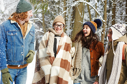 Group of modern young people having fun in winter forest playing with snow and laughing, resort and vacation concept