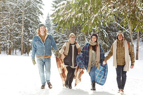 Full length portrait of  happy young people on winter resort running towards camera holding hands  in snowy forest and smiling cheerfully at camera