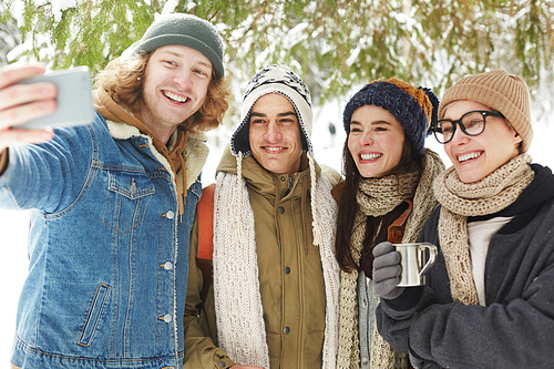 Waist up portrait of  happy young people taking selfie in beautiful snowy forest on winter resort