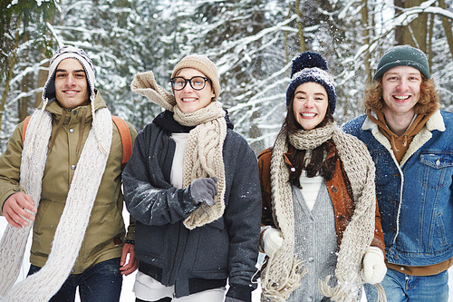 Waist up portrait of carefree young people running towards camera while having fun in winter forest during vacation