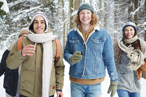 Waist up portrait of four carefree young people running towards camera while having fun in winter forest during vacation, focus on two smiling  men in front