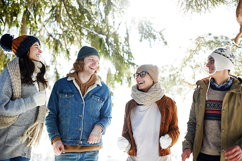 Group of happy young people enjoying walk in beautiful winter forest lit by sunlight on  vacation