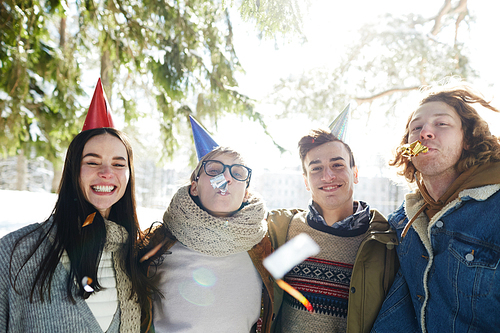 Group of happy young people celebrating Christmas outdoors in beautiful forest, all wearing party caps