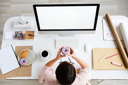 Overview of office manager going to eat donut while sitting by desk in front of computer screen