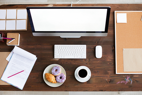 Overview of wooden table with computer monitor, business supplies and snack