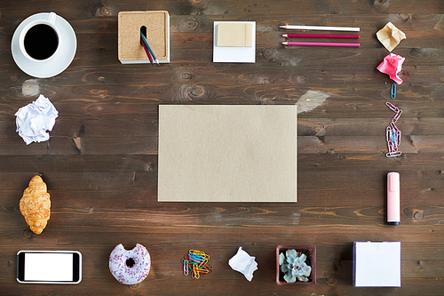 Top view of blank piece of paper, stationery, cup of coffee, pastry and smartphone laid out in rectangular shape on wooden desk
