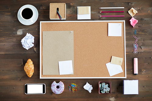Top view of blank cork board, stationery, smartphone, crumpled paper, pastry and cup of coffee on wooden background