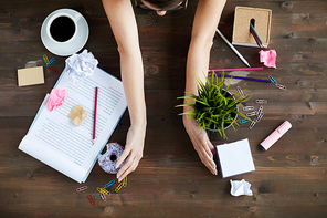 Directly above view of unrecognizable woman sorting out mess on working table, moving stationery, documents, food and plant