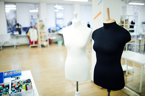 Black and white mannequins placed in spacious fashion studio: threads in containers on table