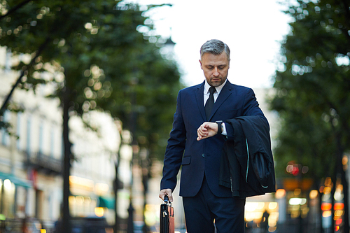 Elegant businessman looking at his watch while moving in the street