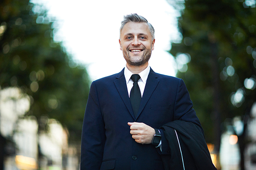 Smiling successful businessman in formalwear looking at you while walking down street