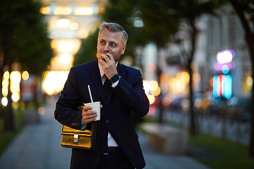Hurrying businessman having sandwich and drink on the move while walking to conference