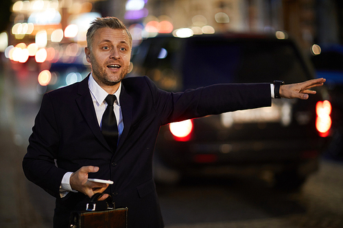 Contemporary businessman with briefcase and smartphone waving for taxi while standing by road