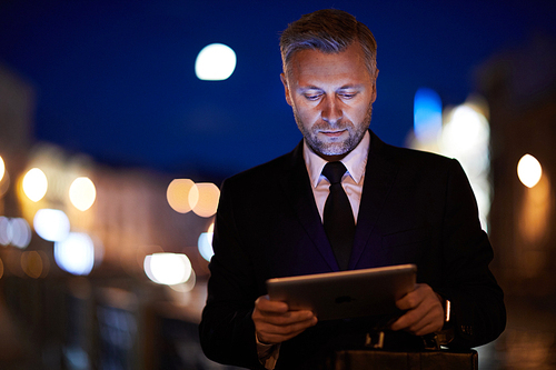 Contemporary mobile businessman with touchpad watching through websites in the evening in urban environment