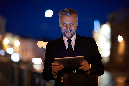 Young successful businessman with mobile gadget reading online news in urban environment