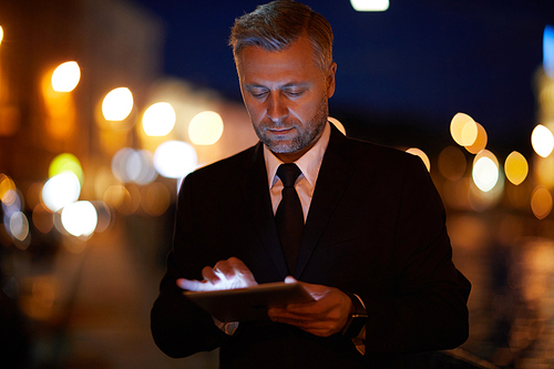 Handsome businessman with tablet searching in the net at night in the city