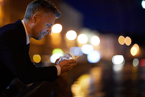 Contemporary businessman messaging or searching in the net outdoors at night after work