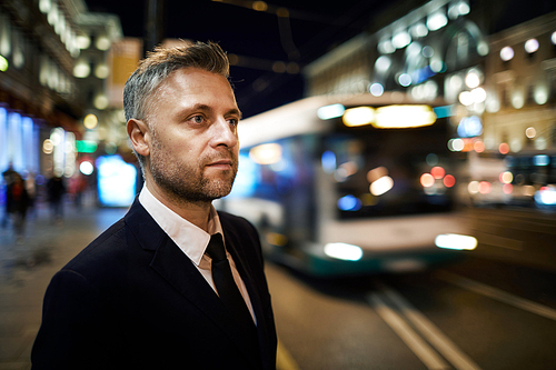 Businessman in elegant suit standing by road and waiting for taxi at night
