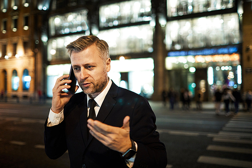 Mature businessman explaining something to one he speaking to on smartphone in urban environment