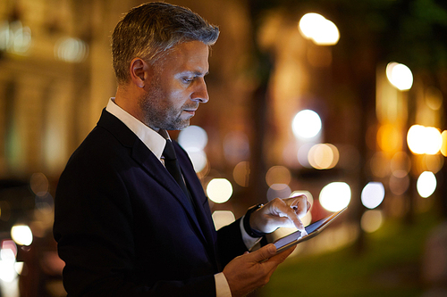 Young businessman with tablet concentrating on networking in the city at night