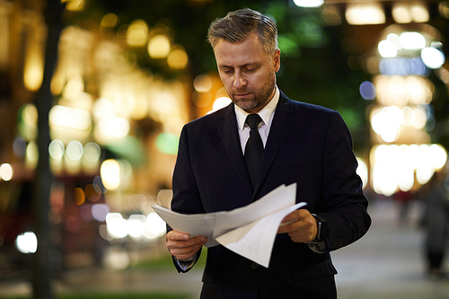 Professional financier looking through papers while walking along street in the evening