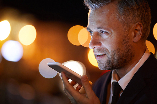 Contemporary businessman recording voice message on smartphone while communicating through mobile app
