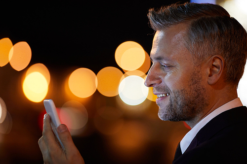 Happy young businessman talking through video-call by smartphone at night