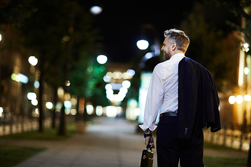 Back view of modern businessman in formalwear chilling in central street at night