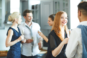 Happy girl with flute of champagne talking to her boyfriend at party on background of friends