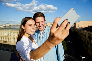 Young affectionate couple  in smartphone while making selfie on roof