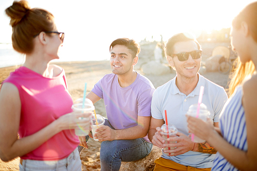Several friendly teens with drinks enjoying hot summer day and picnic on the beach