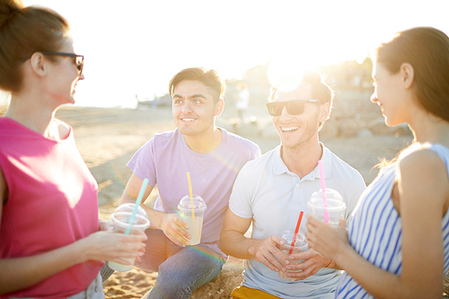 Four casual teens with drinks having fun on the beach on sunny day during summer vacation