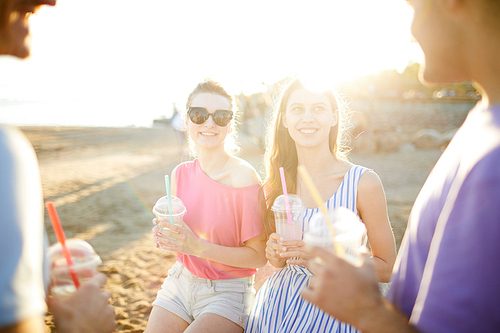 Two smiling girls with drinks talking to their boyfriends on sunny day on the beach