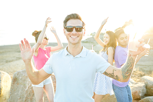 Happy guy with toothy smile dancing on background of friends while enjoying summer day