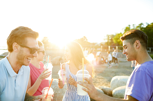 Two happy guys with drinks and their girlfriends on backgrund dancing on the beach