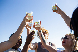 Group of diverse friends holding glasses with beverages while having fun on nice outdoor party.