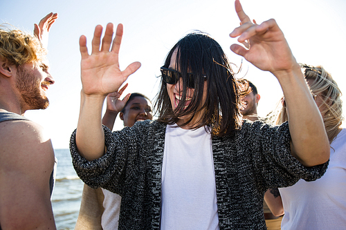 Handsome Asian man in sunglasses dancing among friends while having fun during multiethnic party on beach.