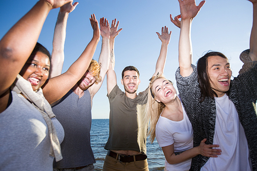 Group of young multiracial people keeping hands up and laughing while having fun during beach party.