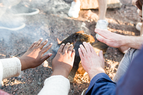 Crop multiracial people warming hands near fire during nice beach party.