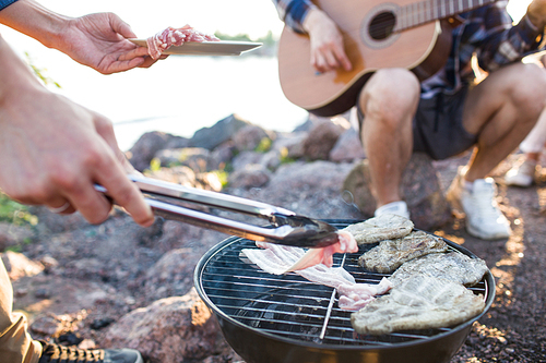 Crop hands of anonymous person grilling delectable meat and bacon during nice beach party.