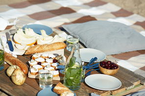 Fruits, fresh bread, sandwiches, bottle and glasses of homemade lemonade and cherries in wooden bowl prepared for party or picnic on the beach