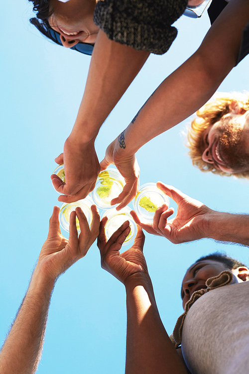 Hands of five friends holding glasses with lemonade and clinking them against blue sky