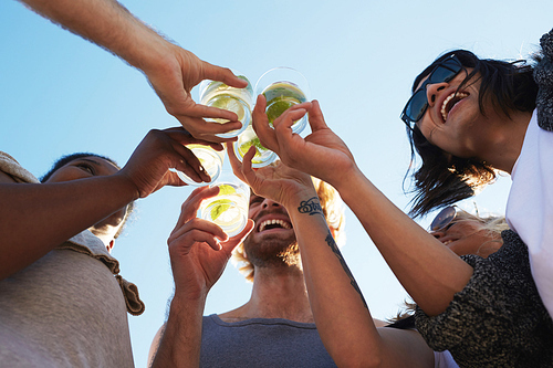 Happy young friends toasting with refreshing drinks under blue sky on summer day