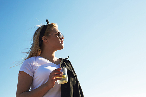 Blonde girl in white t-shirt and eyeglasses holding glass of mojito or lemonade