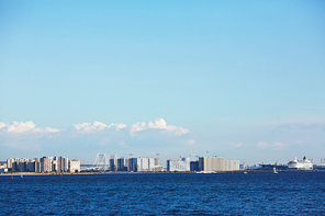 Blue waves of sea and bright sky with cityscape on horizon on hot summer day