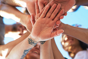 Palms of friends making pile of hands under blue sky outdoors