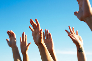 Raised hands of dancing friends enjoying party under blue sky